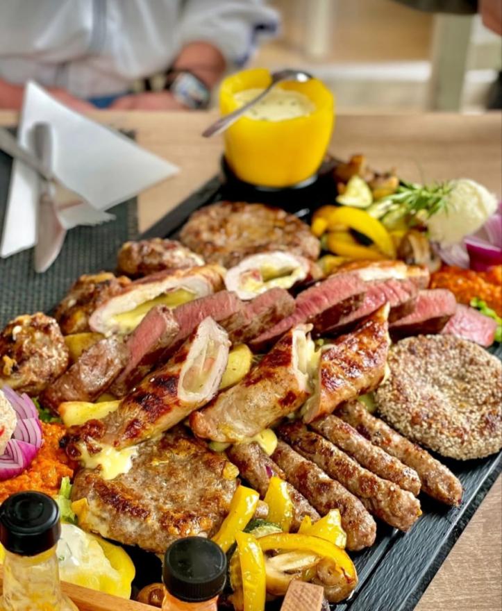 Bogata i raskošna mesna plata s raznim vrstama roštilja, ćevapima, steakom, punjenim mesom, grilanim povrćem i umacima