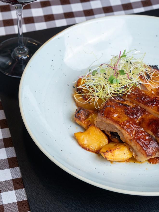 Sočne ploške pečenog mesa s krumpirima i klicama, poslužene na stolu uz čašu crnog vina