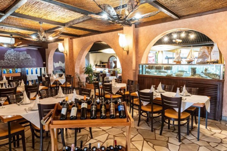 Traditional and cozy interior of Epetium restaurant in Stobreč featuring stone flooring, arched walls, set tables, a wine cart, and a large built-in aquarium