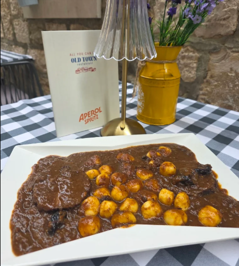 Tradicionalna dalmatinska pašticada s domaćim njokima u gustom tamnom umaku, poslužena na stolu s kariranim stolnjakom uz jelovnik restorana Old Town